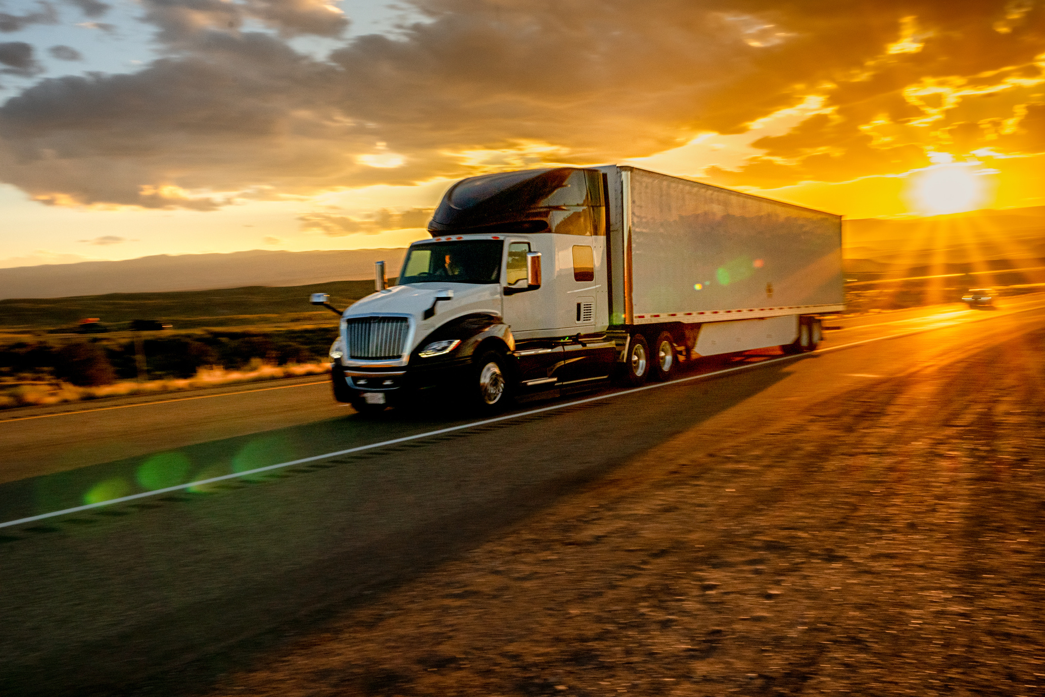 Long Haul Semi Truck Speeding Down a Four Lane Highway in a Beautiful Sunset